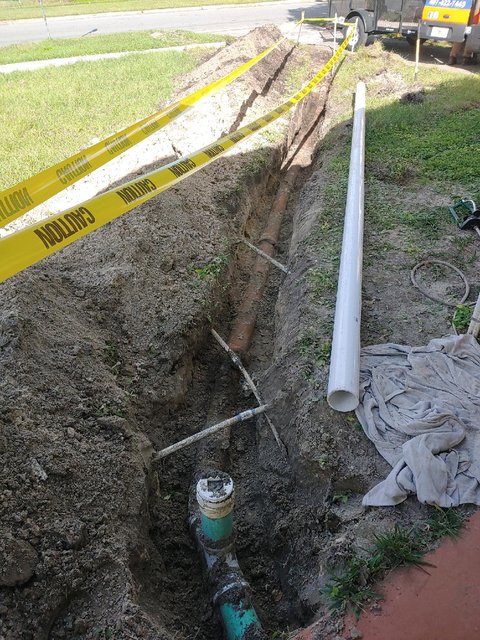 The old clay line exposed in the trench, with new PVC ready to go in