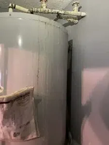 Leaking water heater with visible corrosion and dampness.